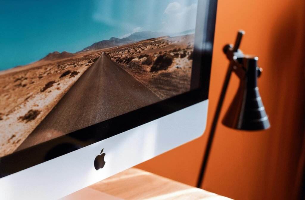 A sleek modern workspace featuring an iMac displaying a desert road and a stylish desk lamp.